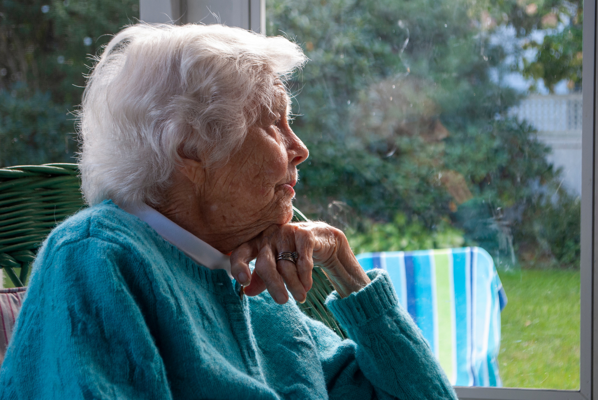 Dreamy elderly woman looking through window in house